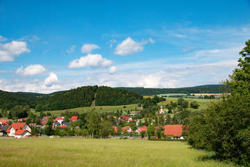 Fototapeta na wymiar sonniges Bergland mit kleinem Dorf Bergen und blauem Himmel