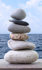 Fototapeta na wymiar Balance Stones stacked to pyramid on wooden floor in the blue sky and sea background.
