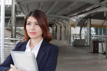 Portrait of attractive Asian secretary holding ring binder at outside office background.