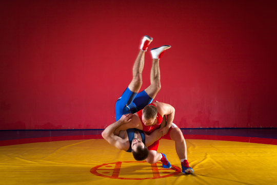 Two strong wrestlers in blue and red wrestling tights are wrestlng and making a suplex wrestling on a yellow wrestling carpet in the gym. Young man doing grapple.