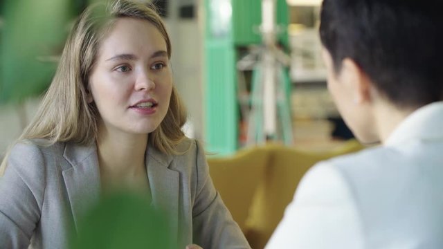 Young woman with long loose hair smiling and talking about herself at a job interview in a caf&eacute;.