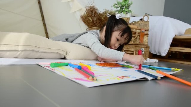 Little asian girl drawing picture by crayon and pencils on the floor at home 
