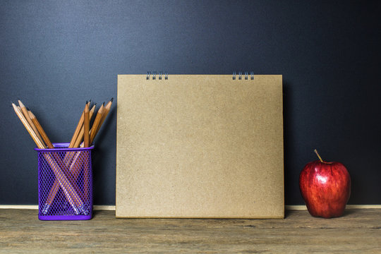 Apple and Pencil on wood table with Empty Brown paper on black background. Education concept.