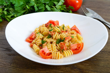 Warm salad with seafood in a white bowl on a wooden background. Pasta Radiatori with crayfish, shrimp, tomatoes, herbs and creamy garlic sauce.