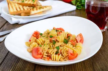 Warm salad with seafood in a white bowl on a wooden background. Pasta Radiatori with crayfish, shrimp, tomatoes, herbs and creamy garlic sauce.
