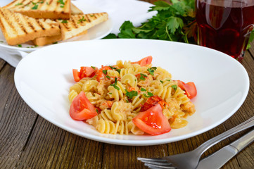 Warm salad with seafood in a white bowl on a wooden background. Pasta Radiatori with crayfish, shrimp, tomatoes, herbs and creamy garlic sauce.