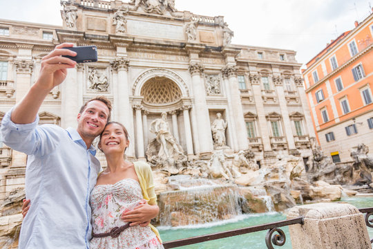 Rome travel tourists couple at Trevi Fountain in Rome, Italy vacation. Happy young romantic couple traveling in Europe taking self-portrait with smartphone camera. Man and woman happy together