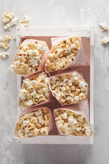 Golden caramel popcorn in pink paper bags in a white wooden box, top view, copy space.