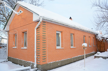 Small Brick House with asbestos roof and roof gutters covered snow.