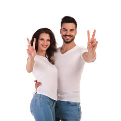 smiling young casual couple making victory or peace sign