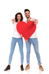 Fototapeta na wymiar young casual couple holding a big heart and points fingers