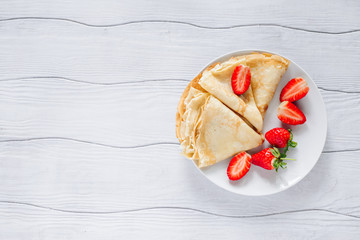 Pancakes with strawberries on a plate on a white wooden table top view