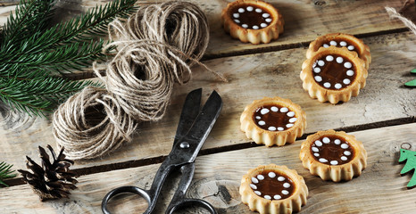 Christmas composition of fir branches, cones, cookies, wooden Christmas toys. In the frame scissors and a skein of braid. Wooden background. Close-up. Macro photography.