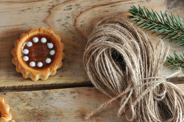 In the frame, a fir branch, a coil of linen rope, a biscuit. A wooden untreated background. View from above. Close-up. Macro photography.