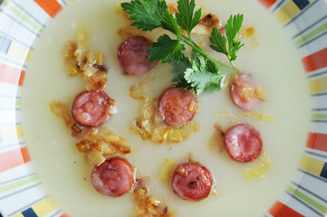 Soup puree from potatoes with smoked sausages and fried onions. The dish is decorated with a sprig of parsley. Wooden light background. View from above.Close-up. Macro photography.