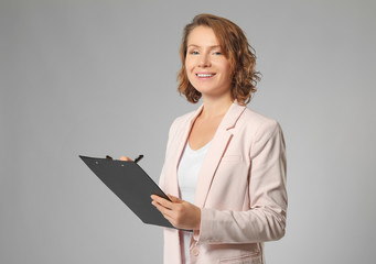 Beautiful real estate agent with clipboard on grey background