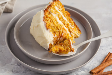 Piece of carrot homemade cake with white cream (cream cheese) on a gray background. Festive dessert concept.