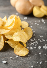 Yummy crispy potato chips with salt on grey table