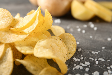 Yummy crispy potato chips with salt on grey table