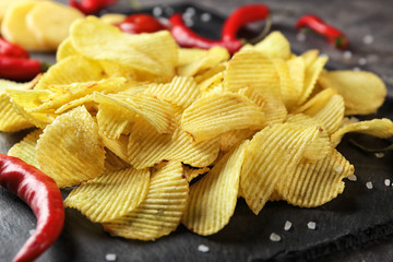 Crispy potato chips with chili pepper on slate plate, closeup