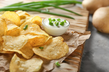 Crispy potato chips with green onion and sour cream on wooden board, closeup