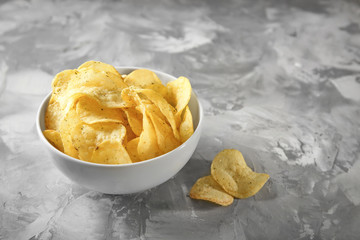 Bowl with crispy potato chips on grey table