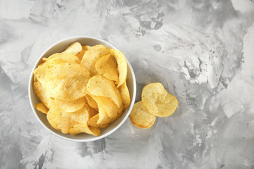 Bowl with crispy potato chips on grey table, top view