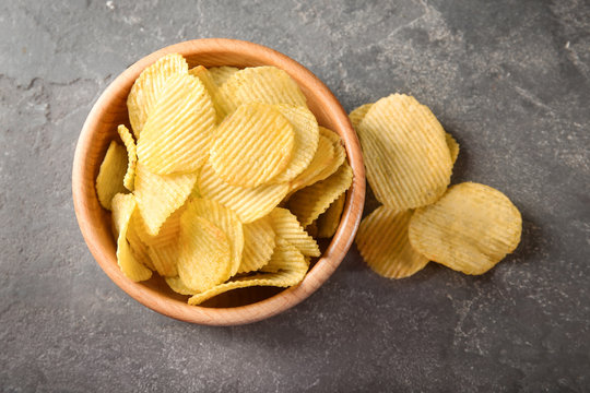 Bowl with crispy potato chips on grey table, top view