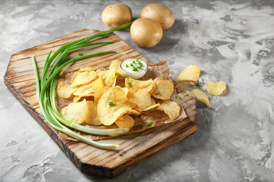 Crispy potato chips with green onion and sour cream on wooden board