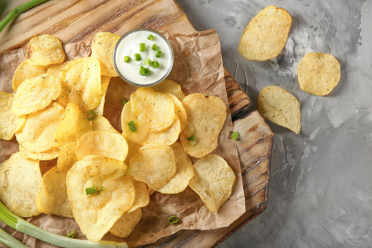 Crispy potato chips with green onion and sour cream on wooden board, top view