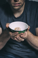 Homeless poor man holding bowl with piece of bread, closeup