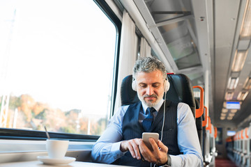 Mature businessman with smartphone travelling by train. - Powered by Adobe