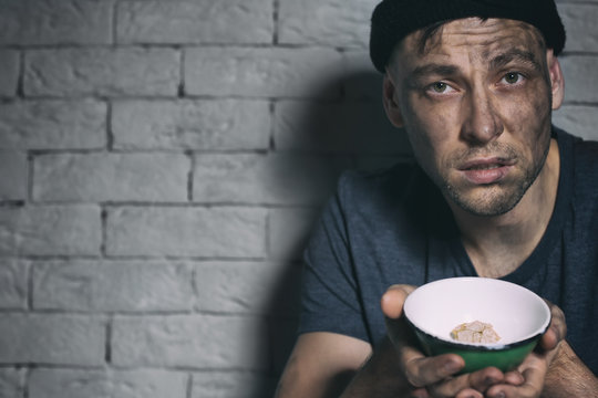 Homeless poor man holding bowl with piece of bread near brick wall