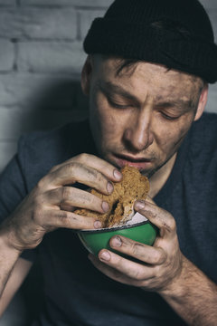 Hungry poor man eating piece of bread against brick wall