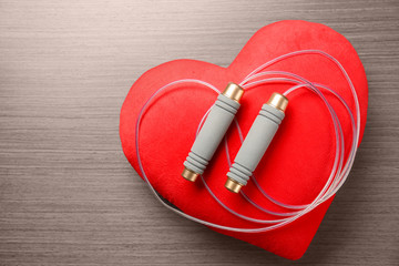Jumping rope and red heart on wooden background. Cardio training concept