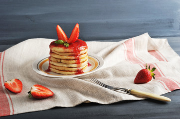 On a plate of pancakes, poured with strawberry jam and decorated with fresh strawberries. In the...