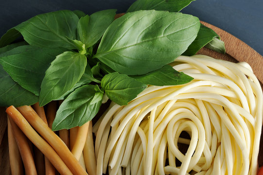 Figured Chechel cheese in the form of spaghetti and in the form of smoked straws on a wooden dish. Next to the green of the basil. Dark background. Close-up. View from above. Macro photography.