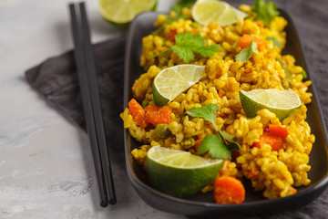 Vegetarian curry rice with vegetables and coconut cream in a black plate. Gray background, copy space. Healthy vegan food concept, detox, vegetable diet.