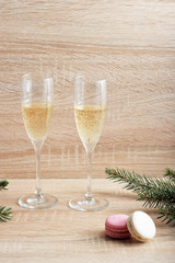 Two glasses with champagne and pasta macaroons. Spruce branches give the composition a Christmas character. Light background. Vcrtical orientation of the frame. Close-up.