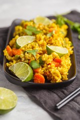 Vegetarian curry rice with vegetables and coconut cream in a black dish. Gray background, copy space. Healthy vegan food concept, detox, vegetable diet.