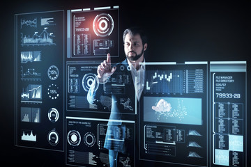 Obraz premium Careful programmer. Attentive experienced smart programmer looking elegant in his suit while standing in front of a futuristic device and touching the screen of it