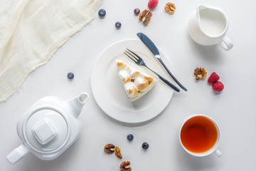 top view of piece of cake with berries and tea on white table