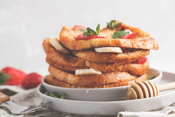 French toasts with honey, banana and strawberries on gray plate. Gray background