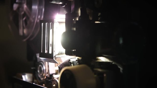 Movie projector super 8mm running tracking shot focused on lens and light on dark background