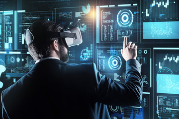 New equipment. Clever progressive young programmer feeling clam while wearing necessary virtual reality glasses and touching the screen of a transparent computer