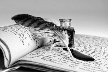 Old writing feather and ink spot with handwritten letter in background, black and white
