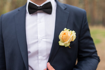 Wedding boutonniere with yellow rose on suit of groom. Groom in blue jacket, white shirt and black tie with boutonniere. Wedding details