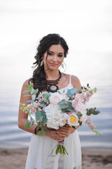 bride in a boho style on the beach near the sea with a wedding bouquet