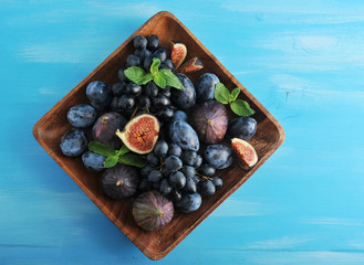 Ripe plums, grapes and juicy figs on a square dish. Composition is supplemented with mint leaves. Blue wood background. Close-up. Macro photography.