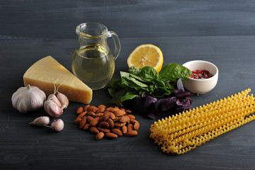 Ingredients for pasta with pesto sauce. In the frame, green and purple basil, almonds, half a lemon, parmesan cheese, garlic, spices, olive oil and pasta. Dark background. Close-up.